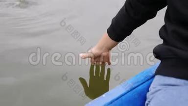 小女孩轻轻地摸着湖面上的水。 女人在绿水上牵着手掌。 女人的手在公园里碰水。 女汉